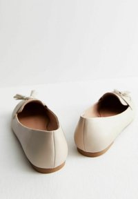 Beige leather ballet flats with a smooth texture, round toe, and a bow accent on the heel. Flexible sole with a light brown base.