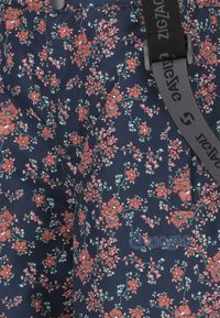 Blommönstrad tyg i marinblått med rosa och gröna blommor. Har en svart justerbar rem och broderad "ZIGZAG"-logotyp.