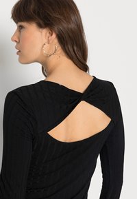 Top preto com textura canelada e design torcido nas costas, apresentando um detalhe de costas abertas. As mangas longas e a textura suave aumentam o conforto.