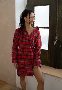 Rood geruit hemdjurkje met lange mouwen, knoopsluiting aan de voorkant en een losse fit. Beschikt over een gespleten zoom en stof van gemiddelde dikte in een blokpatroon.