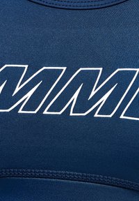 Marinblå tränings topp tillverkad av texturerat tyg, med stor vit text och prydlig söm längs fållen och kragen.