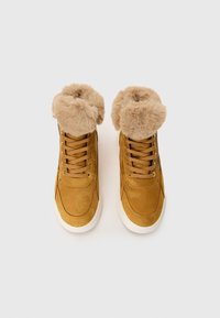 Brune suede høyde sneakers med faux pels mansjett, beige snørebånd og hvit gummisåle. Teksturert materiale med sømdetaljer.