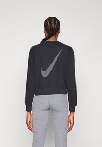Sweat-shirt noir au design court, avec un logo Nike rayé vertical au dos. Poignets et ourlet côtelés, associé à des leggings gris.