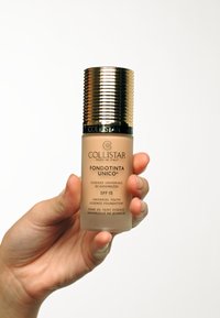 Flacon de fond de teint Collistar avec un corps beige givré et un capuchon doré strié. Le texte comprend "FONDOTINTA UNICO®" et "SPF 15."