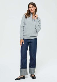 Sweat-shirt gris clair avec un design à demi-zip, associé à un jean large bleu foncé avec des poignets contrastants. Des mocassins noirs complètent le look.
