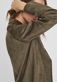 Olivi vihreä mokkanahkainen pitkähiha jacket, jossa on notch-kaulus ja hienovaraiset ompelutiedot. Kankaassa on pehmeä rakenne ja sileä pinta.