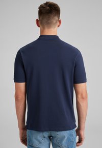 Polo de color navy con mangas cortas y cuello de punto plano. Tejido suave y texturizado con un dobladillo recto. Se lleva con jeans de mezclilla azul claro.
