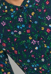 Skjorta med blommönster som har en marinblå bakgrund med färgglada blommor i rosa, gult, blått och grönt, komplett med svarta knappar.