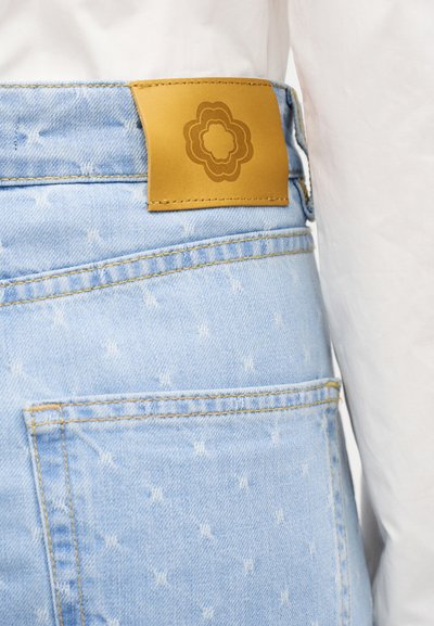 Φωτεινό γαλάζιο τζιν με μικρές λευκές κεντητές τελίτσες, με ταμπά δερμάτινο ταμπελάκι με λουλουδένιο λογότυπο στη μέση.