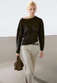 Zwarte oversized trui met een bootnek, lichtgrijze rechte broek en een kleine donkergbruine handtas met een omgevouwen klep.