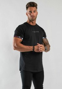 Svart t-shirt med kort ärm och grafisk "LIMITÉ"-tryck på framsidan, med mönstrade detaljer på ärmarna och en åtsittande design.