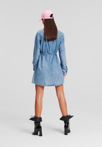 Denim obleka s pripetim pasom, dolgimi rokavi in ukrivljenim robom. V kombinaciji s sijočimi črnimi gležnjarji in roza kapo.
