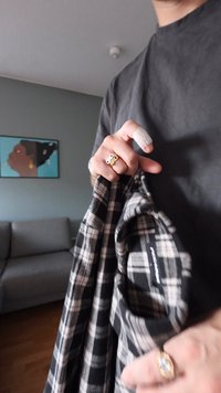 Svartvit rutig flanellskjorta hålls i en hand med en guldring som har ett band och en ädelsten, och ett finger lindat i ett bandage.