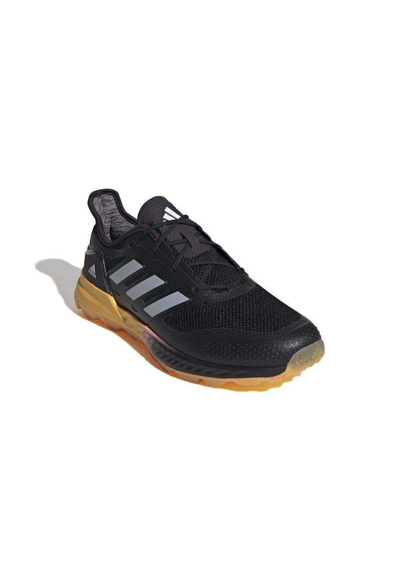Chaussure de sport noire avec tige en maille, accents argentés et semelle texturée robuste. Comprend un col rembourré et un système de laçage.