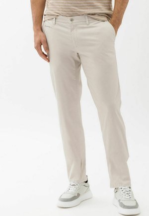 Light beige cotton pants with a straight-leg design, featuring front pockets and a metal button closure, paired with white sneakers.