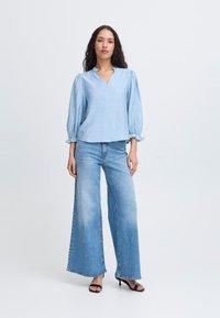 Ljusblå blus med puffärmar och V-ringning. Matchas med vida ljusblå jeans. Slät tygtextur, minimala designinslag.