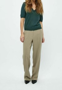 Top de punto verde con escote en V y mangas cortas, combinado con pantalones beige de pierna ancha y zapatos planos negros de punta. Sutil textura en el top.