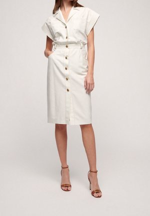 Valkoinen puuvillamekko, jossa on lyhyet, laskostetut hihat, edestä napillinen sulkeminen, kaksi taskua ja vyötärövyö. Yhdistetty hihnallisiin korkeakorkoisiin sandaaleihin.