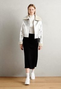Zilveren nepbontjas met een pluche kraag, ritssluiting en twee zijzakken, gecombineerd met een zwarte midi-rok en witte sneakers.