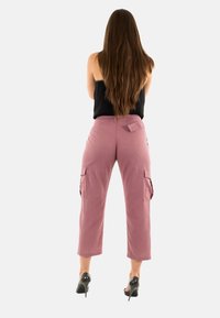 Pantalones cargo en un color rosa polvo, con bolsillos laterales, un corte holgado y una longitud recortada. El material parece ligero con un acabado texturizado.