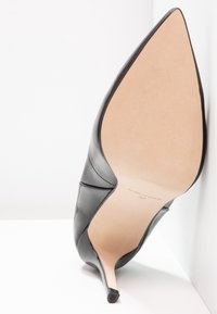 Talons aiguilles en cuir noir avec bout pointu. Texture lisse et design minimaliste. Semelle claire avec texte gravé.