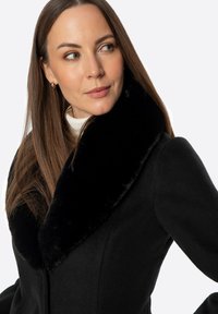 Czarny płaszcz z pluszowym, czarnym kołnierzem z imitacji futra, dopasowany fason, gładka tekstura, długie rękawy, cechujący się wyraźną konstrukcją i czystymi liniami.