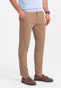 Brązowe spodnie slim-fit z dwoma bocznymi kieszeniami, wykonane z lekkiego materiału, w połączeniu z brązowymi butami typu mokasyn.