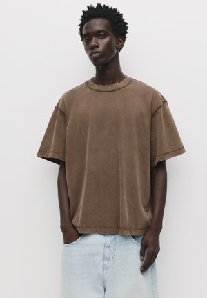 Brun oversized T-shirt lavet af blød bomuld, med rund hals, korte ærmer og en afslappet pasform. Let syning er synlig.