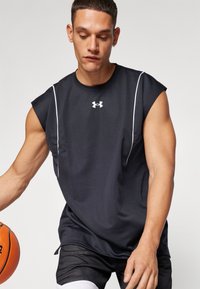 Fekete ujjatlan sportpóló texturált felülettel, fehér kiegészítőkkel és Under Armour logóval. A modell kosárlabdát tart, mintás rövidnadrágot visel.