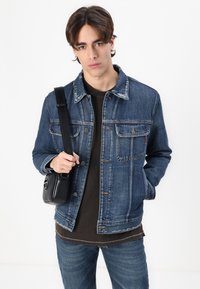 Denim jacket in dark blue with a classic cut, two front pockets, and button closure. Black crossbody bag with a smooth texture.