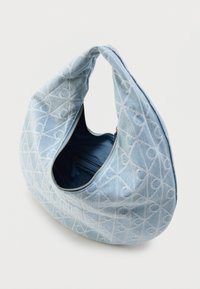 Τσάντα ώμου από τζιν σε ανοιχτό μπλε χρώμα, με αφηρημένο μοτίβο, κυρτό σχήμα και επάνω φερμουάρ. Εσωτερικά επενδεδυμένη με σκουρόχρωμο μπλε ύφασμα.