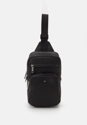 Schwarze Leder-Crossbody-Slingtasche mit verstellbarem Riemen, drei Reißverschlussfächern und kleinem Metalllogo auf der Vordertasche.