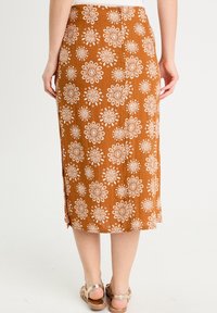 Bronze midi kjol med blommönster, figursydd midja, vita blommönster, sidoflik och texturerat tyg. Matchas med ljusa sandaler.