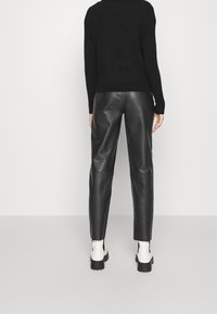 Svart stickad tröja i kombination med svarta läderbyxor. Byxorna har rak skärning och en slät textur. Vita ankelboots visas.