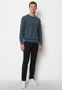 Blauer Strickpullover mit Rundhalsausschnitt, getragen mit schwarzen Hosen und weißen Sneakers. Glatte Textur, enges Design und keine sichtbaren Muster.