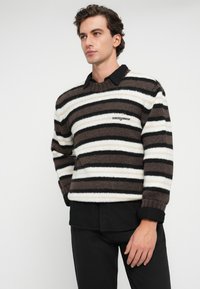 Ριγιέ ζακέτα σε καφέ, κρέμ και μαύρο πλέξιμο με ριμπ ύφανση. Διαθέτει στρογγυλή λαιμόκοψη και κεντημένο λογότυπο "tommy jeans".