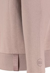 Light pink sweater with a smooth texture, ribbed hem, and branding tag. Features subtle logo accents on the sleeve near the cuff.