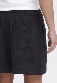 Schwarze Shorts aus strukturiertem Stoff mit einer aufgenähten, rechteckigen Gesäßtasche. Verfügt über einen elastischen Bund und ein gerade geschnittenes Design.