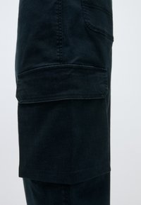 Σκοτεινές τζιν cargo παντελόνες με κανονική εφαρμογή, διαθέτοντας μία μεγάλη πλαϊνή τσέπη, λείο ύφασμα και αντίθετο ραπτό στις ραφές.