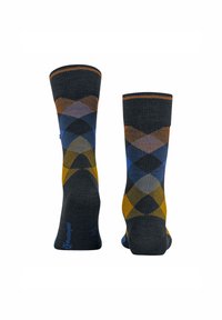 Des chaussettes foncées affichent un motif argyle en diamants bleus, orange et jaunes. Le design est distinctif et coloré, idéal pour un style décontracté.
