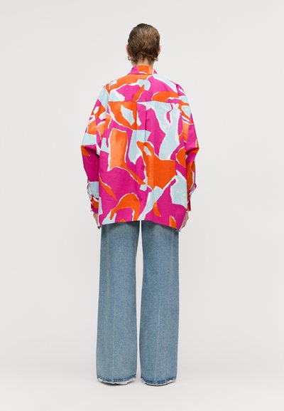 Colorful oversized shirt featuring a mix of pink, orange, and light blue abstract patterns. Fabric appears smooth; design is casual and relaxed.