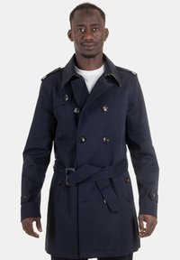 Cappotto trench navy con chiusura doppiopetto, grandi bottoni, spalline e cintura. Realizzato in un tessuto liscio e strutturato.
