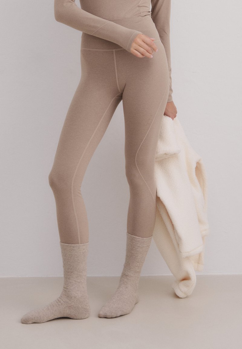 Beige leggings met naaddetails, gecombineerd met lichtbeige sokken en een witte gebreide trui. Glad materiaal, aansluitend ontwerp.