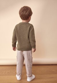Groene gebreide trui met een ronde hals, gecombineerd met lichtbeige cargobroek en witte sneakers, gezien van achteren.