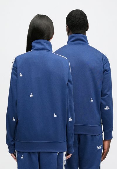 Modré pulóvre mikiny s vysokými goliermi, zdobené bielou výšivkou králika a kontrastnými bočnými pruhmi. Mäkká textúra a pohodlný strih.