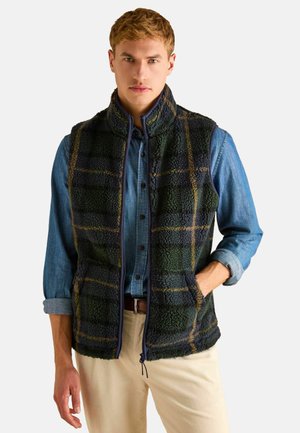 Fleece-Weste mit grün-blauem Karomuster, hohem Kragen, Reißverschluss und Seitentaschen, darüber ein Jeanshemd.