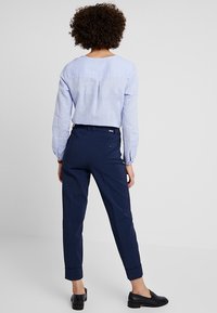 Ljusblå långärmad skjorta med rund halsringning och veckdetalj baktill, kombinerad med marinblå taperade byxor och svarta loafers.