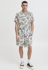 Ensemble chemise à manches courtes à col et short couleur crème avec motif floral bleu marine. Comprend des poches, une coupe décontractée et un tissu texturé.