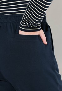 Marina bomullsjoggers med elastisk midja, med sidofickor och en mjuk yta. Randig långärmad topp med marina och krämfärgade linjer.