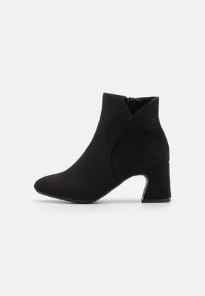 Sorte faux suede ankelstøvler med spids tå, mellemhøj blokhæl og lynlås i siden; glat tekstur og minimale sømdetaljer.